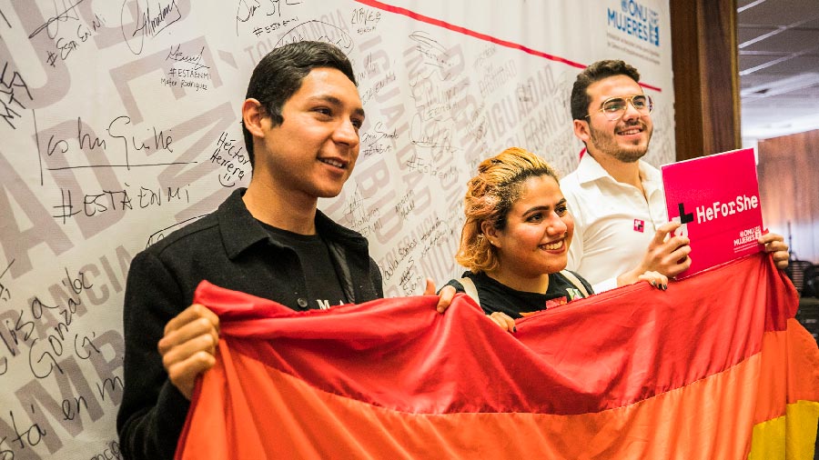 Jóvenes con la bandera LGBT+ y un cartel de HeForShe