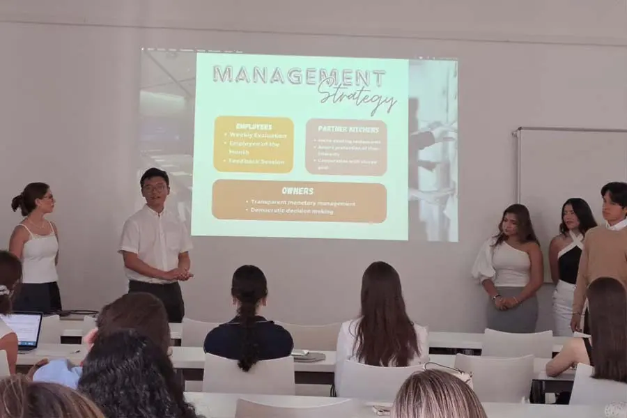 5 alumnos presentando al frente de un salón de clases. 