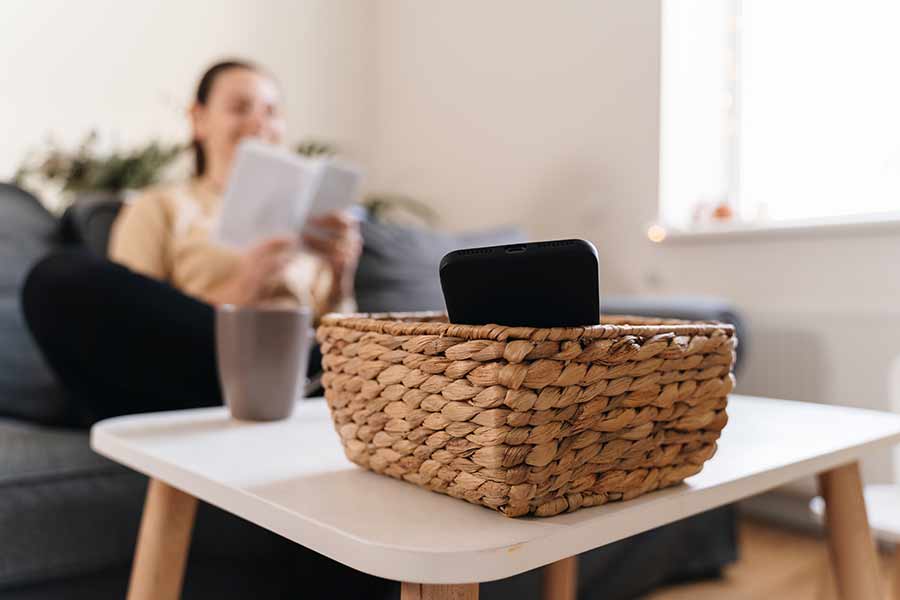 Mujer leyendo un libro y sobre una mesa, a lo lejos, su celular