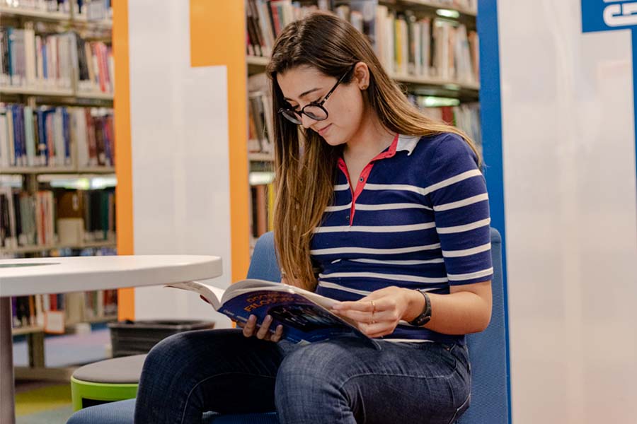 alumna becada leyendo un libro en biblioteca