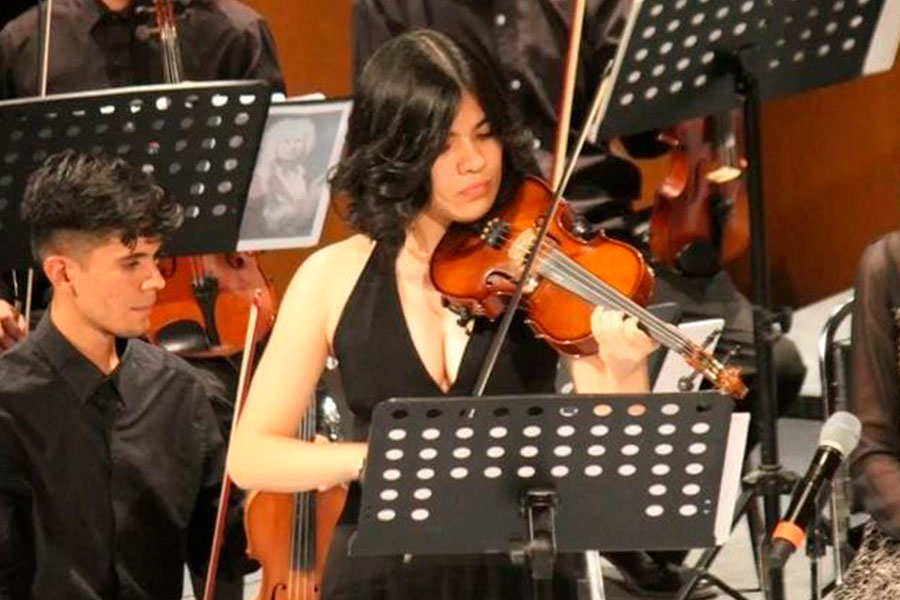 Joven mujer vestida de negro hace música tocando el violín en una orquesta