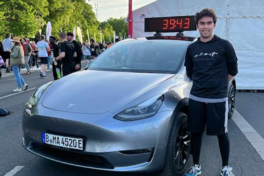 Alumno posando frente a automóvil Tesla en exposición de la marca  