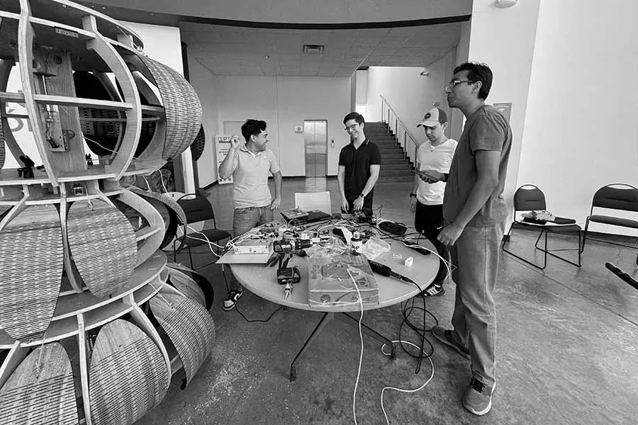 Cuatro jóvenes frente a una mesa con equipo técnico y una escultura al lado.