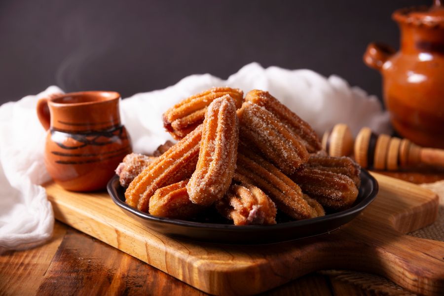 Churros mexicanos sencillos cubiertos de azúcar y canela, servidos en un plato con jarrito de barro, un postre típico en celebraciones navideñas.