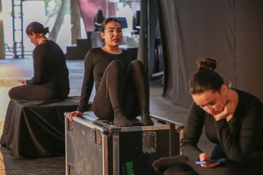 Tres j&oacute;venes vestidas de negro sentadas sobre cajas negras en un escenario. 