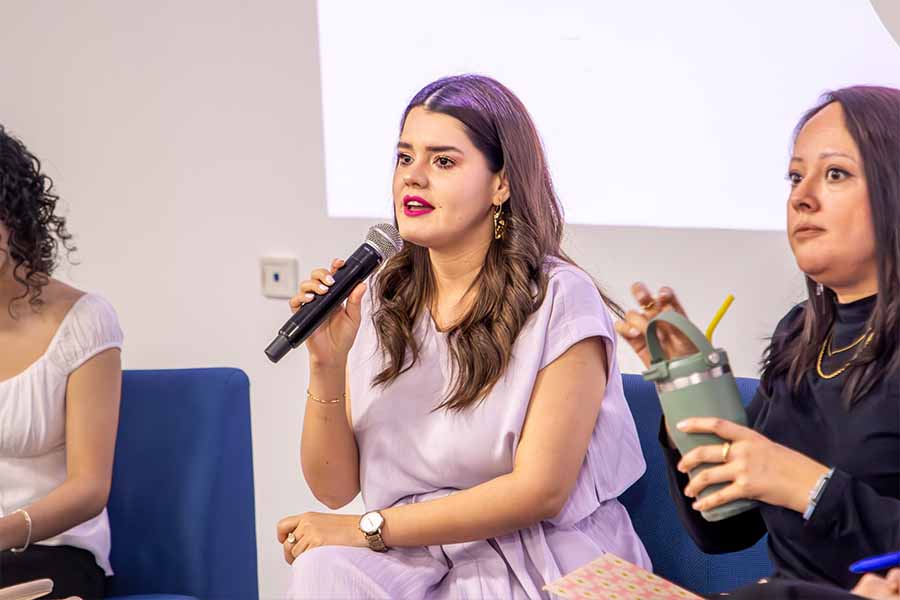 Mujer hablando frente a p&uacute;blico con micr&oacute;fono.