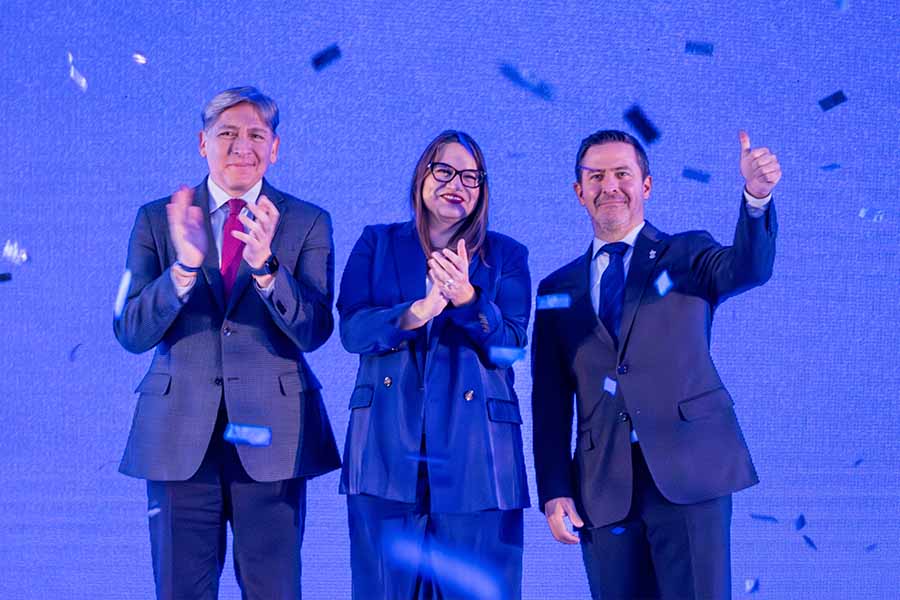 Tres personas aplauden frente a una pantalla mientras cae confeti alrededor. 