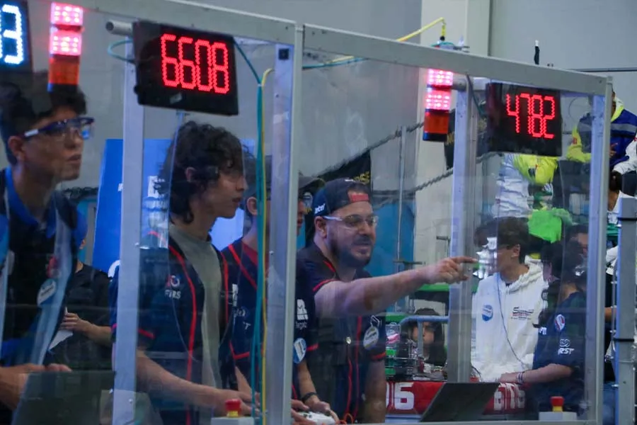 Dos alumnos y su coach detrás en la estación de manejo para controlar el robot durante la competencia. 