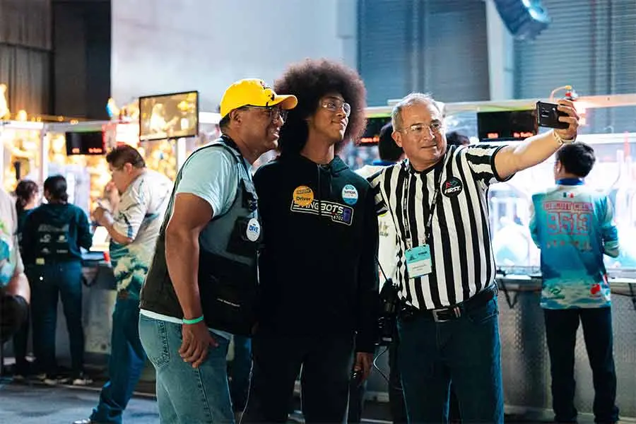 Un miembro del equipo StingBots 6702 de PrepaTec Santa Anita posa para una foto con un voluntario y un árbitro de FIRST Robotics Competition durante el regional en México.