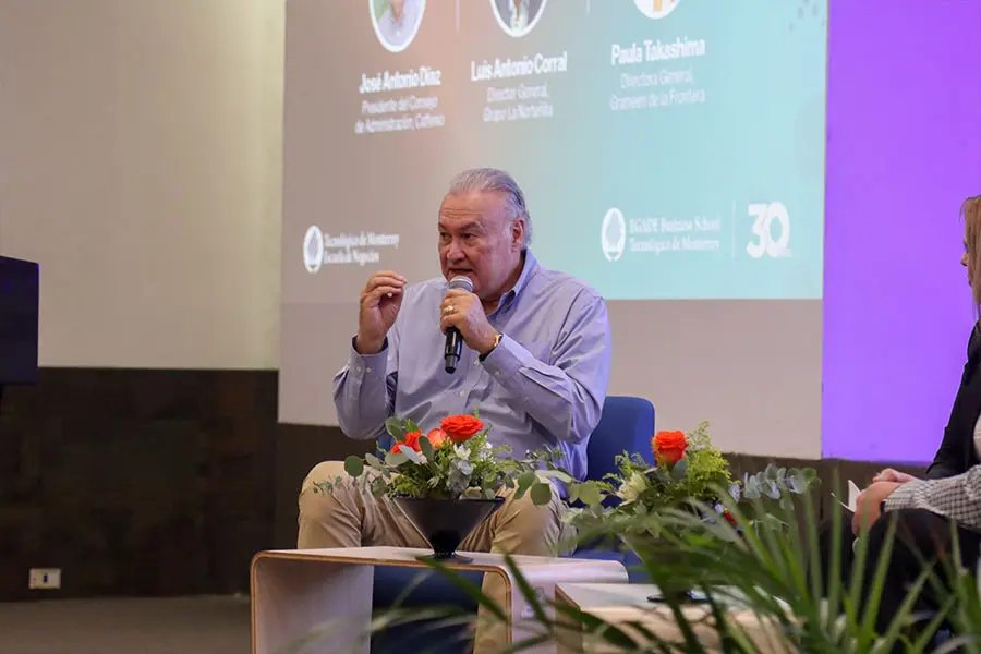 Hombre sentado en escenario hablando al público. 