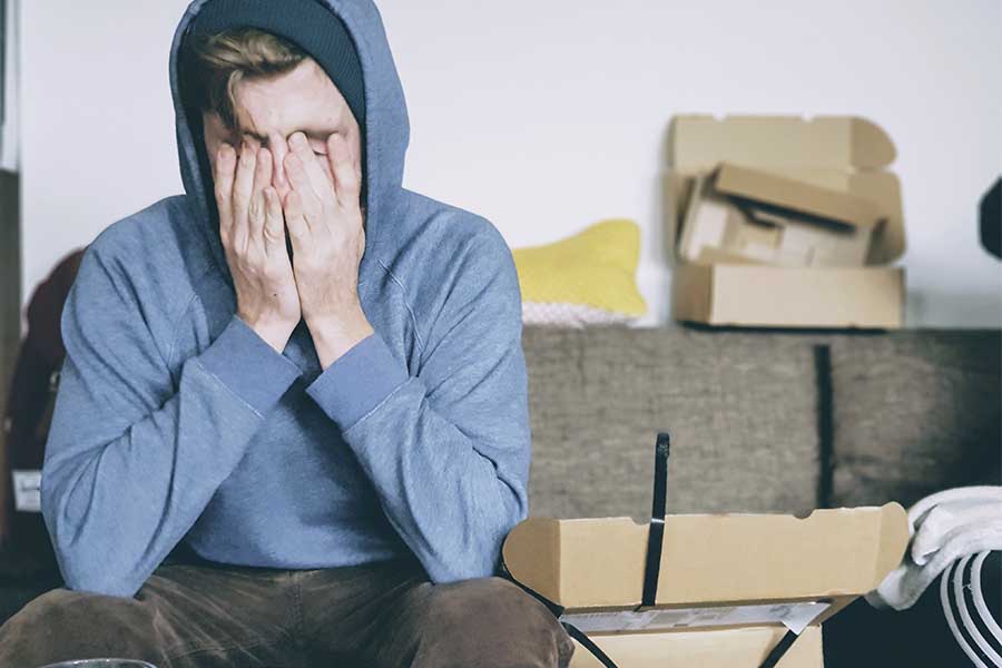 Joven con sudadera azul en un cuarto, con las manos en la cara  y estresado