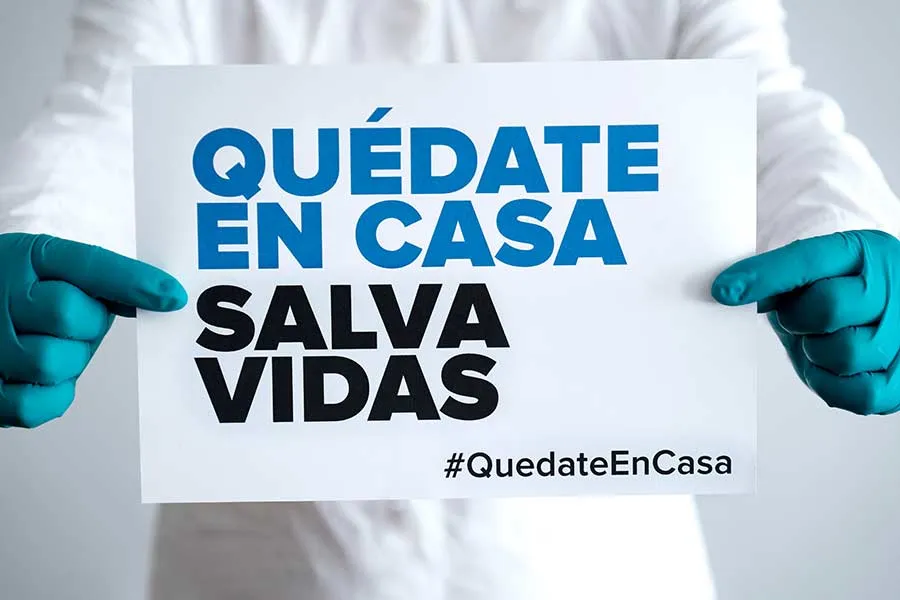 Manos sosteniendo un letrero con el mensaje: "Qu&eacute;date en casa, salva vidas"