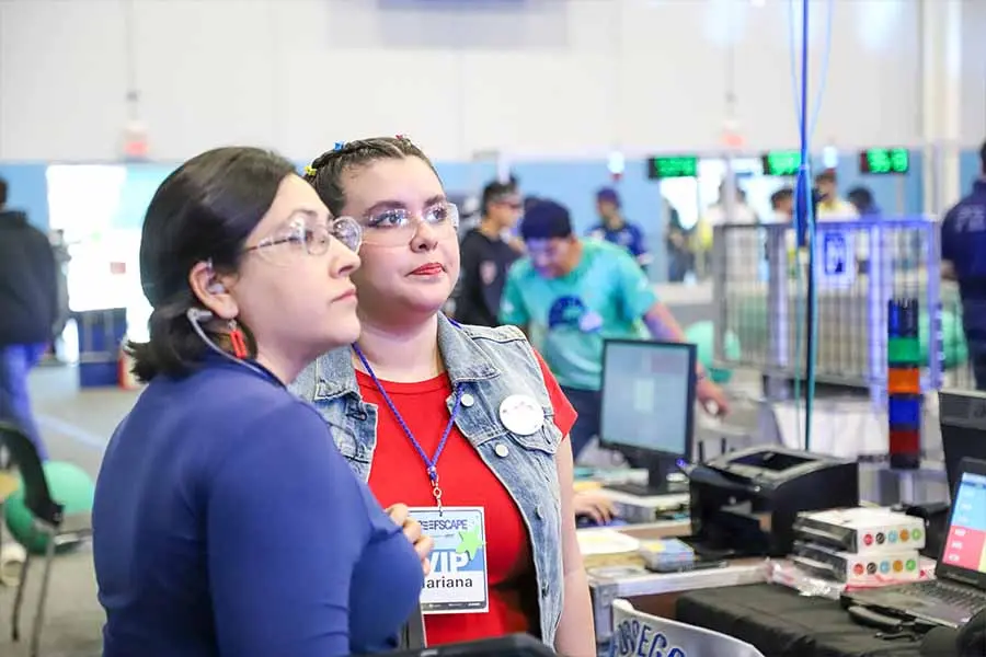 Foto del perfil de una profesora y una alumna mirando hacia una pantalla fuera de cuadro.