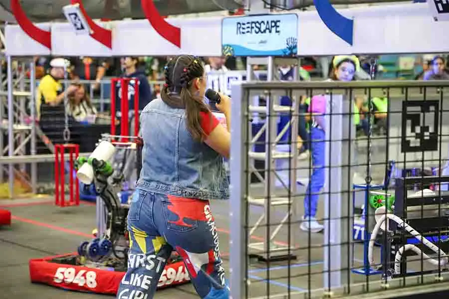 Vista de espaldas de una jovén en la cancha de FIRST presentando a los equipos.