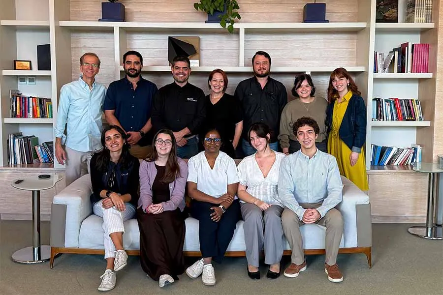 Grupo de 12 personas de g&eacute;neros y edades variadas, posando en grupo frente a un librero.