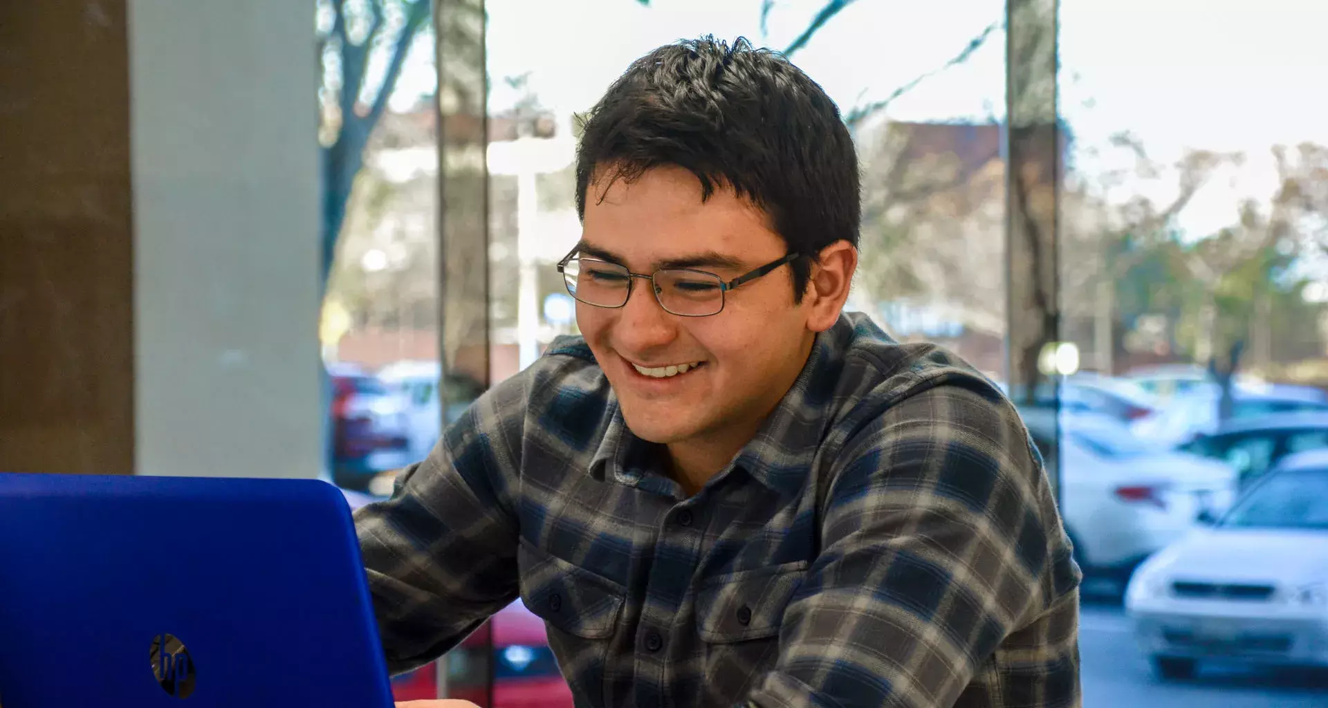 Joven sonriendo mientras observa la pantalla de su computadora portatil