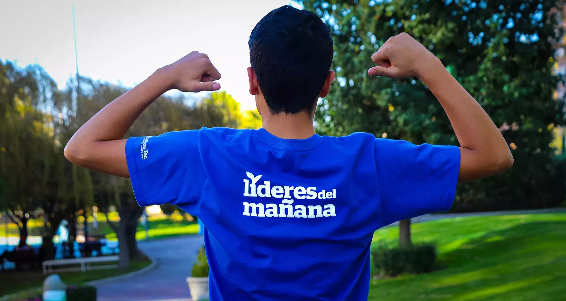 Chico de espaldas señalando la playera que dice: Líderes del Mañana