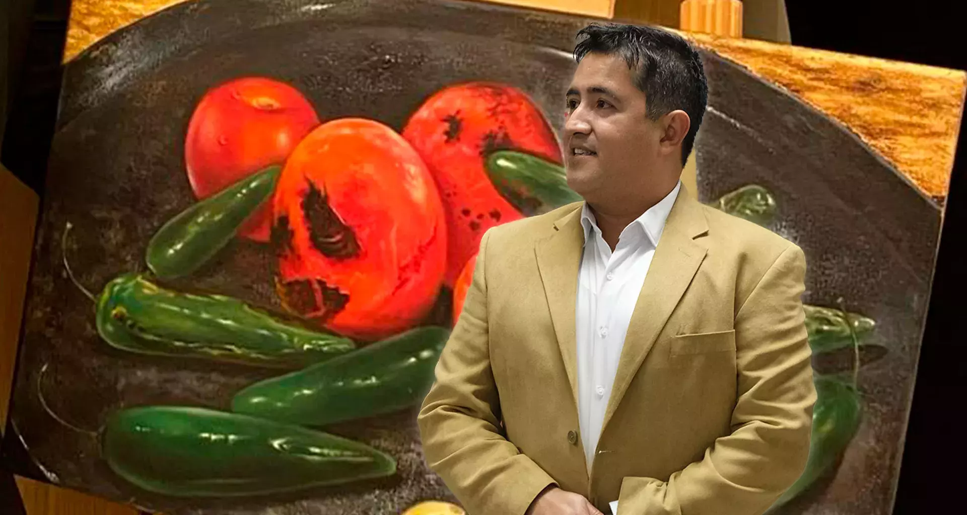 Profesor de arte usa traje color café y de fondo tiene una de sus pinturas en óleo con tomates y chiles