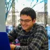 Joven sonriendo mientras observa la pantalla de su computadora portatil