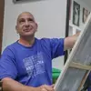 Profesor de artes plásticas pintando un cuadro con ligera sonrisa volteando hacia arriba.