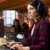 estudiante universitaria con audifonos viendo varias pantallas 