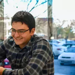 Joven sonriendo mientras observa la pantalla de su computadora portatil