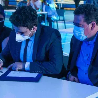 Alumno firmando su título profesional, sus padres a su lado apoyándolo.