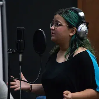 Vista de perfil de una mujer con audífonos hablando en frente de un micrófono. 