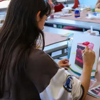 Vista de espaldas de una alumna pintando un pastel en un lienzo.