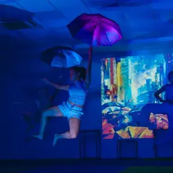 Tres bailarinas saltando mientras cada una sostiene una sombrilla en su manos.