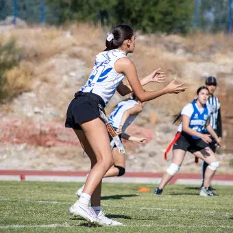 Jugadora de tocho en posición para recibir un balón de fúbtol americano que viene hacia ella. 