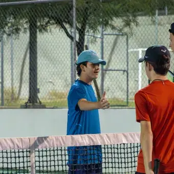 Tres jugadores de tenis se dan la mano al centro de la cancha. 