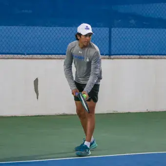 Un jóven sostiene una raqueta de tenis en una mano y una pelota de tenis en la otra mientras prepara su saque. 