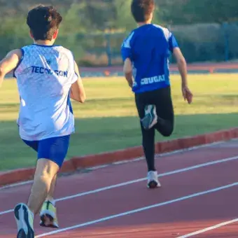 Vista de espaldas de dos atletas corriendo en una pista de atletismo. 