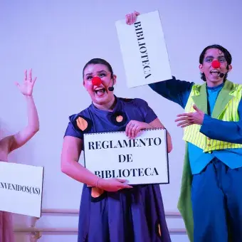 Actores con vestuarios y narices de payaso sosteniendo letreros. 