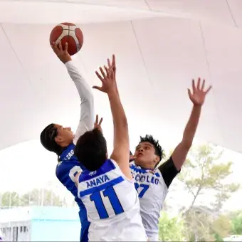 Jugadores de básquetbol saltando hacia el aro para una entrada a canasta durante una jugada ofensiva.