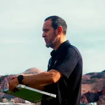 Entrenador de un equipo de futbol varonil observa el desempeño de sus pupilos mientras toma nota teniendo como fondo los cerros de Chihuahua.