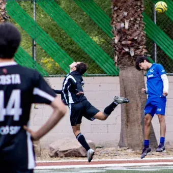 Dos futbolistas disputando la posesión del balón con fuerza y determinación en el campo de fútbol.