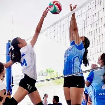 Dos jugadoras saltando frente a la red para realizar ataque y bloqueo en un partido de voleibol.
