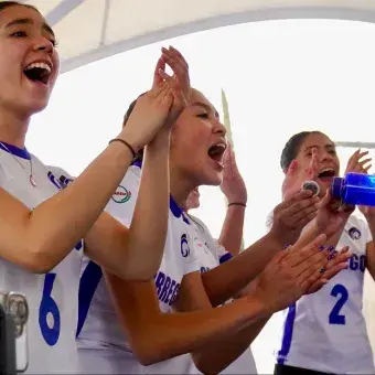 Grupo de jugadoras de voleibol en la banca celebrando con euforia un punto obtenido.